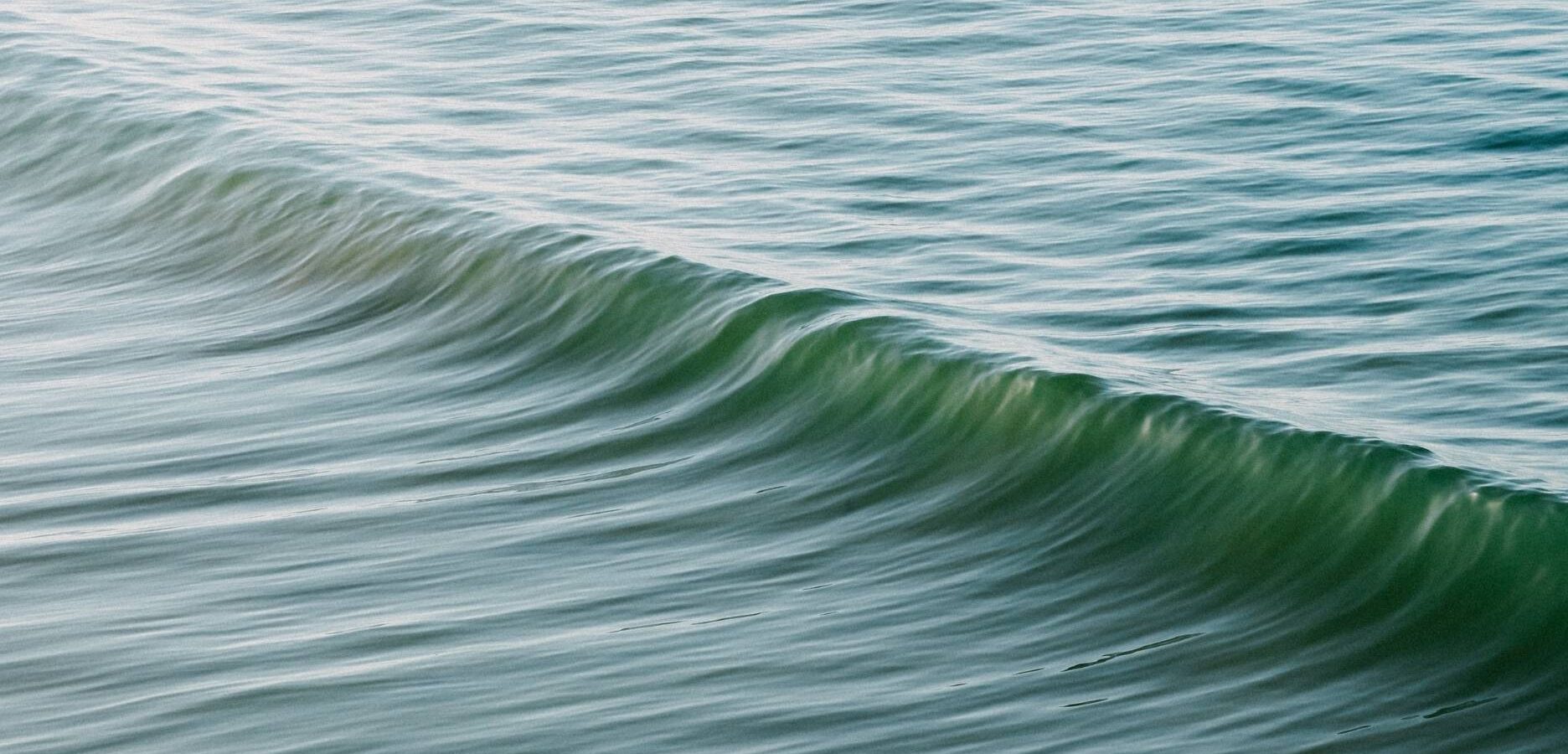A close-up view of gentle ocean waves with soft ripples and greenish-blue water under natural daylight.