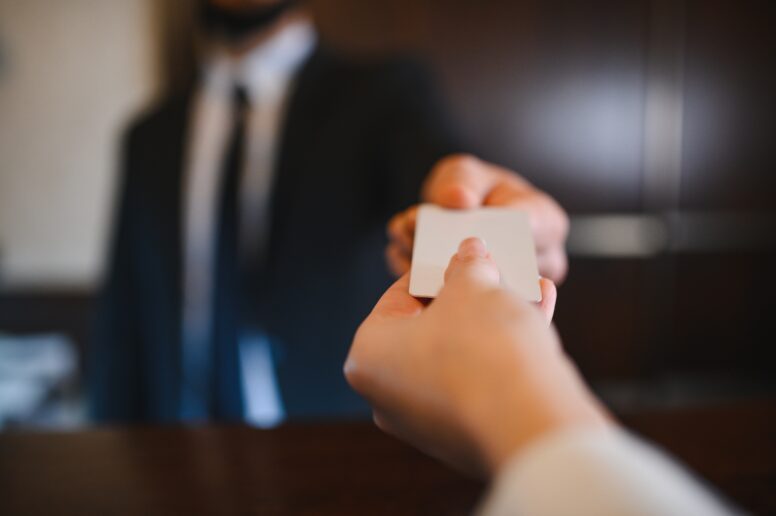 Close-up of a person handing a blank card to another person, both in professional attire, with a blurred background.